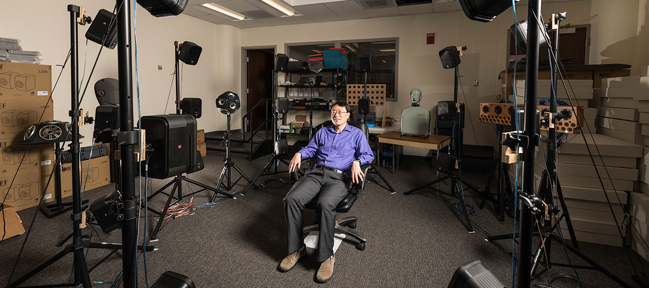 A professor sitting in a chair surrounded by equipment.