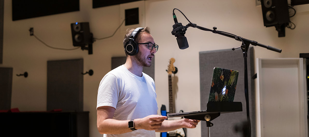 A student standing in front of a microphone making a recording.